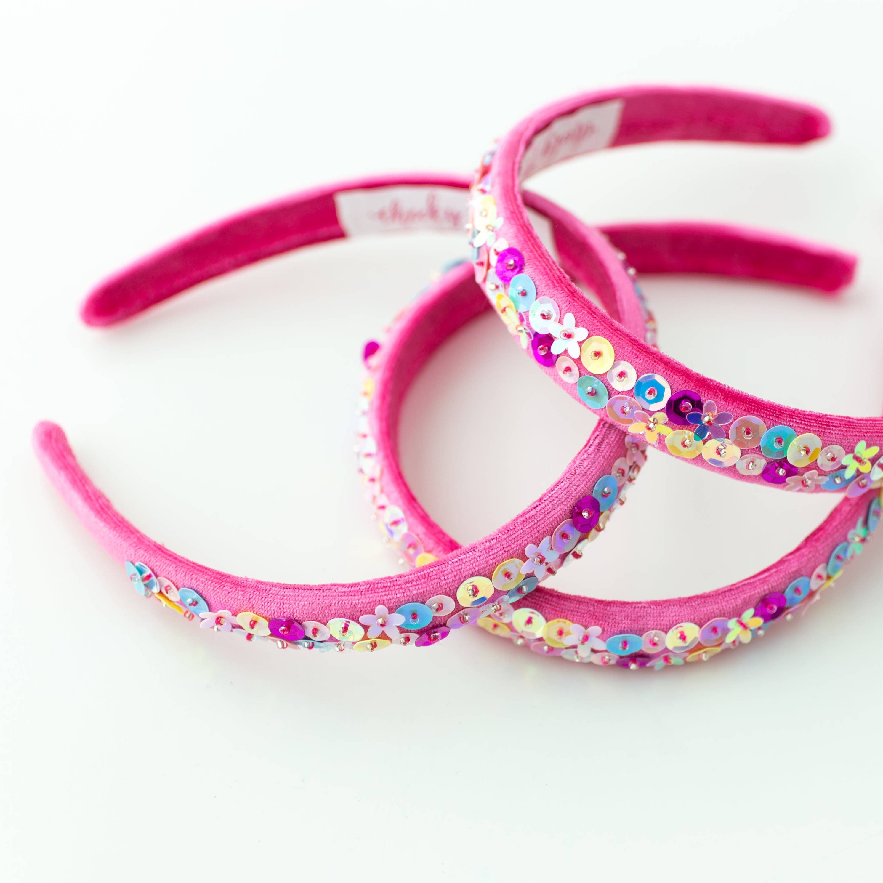 Three pink headbands with floral embellishments on a white background