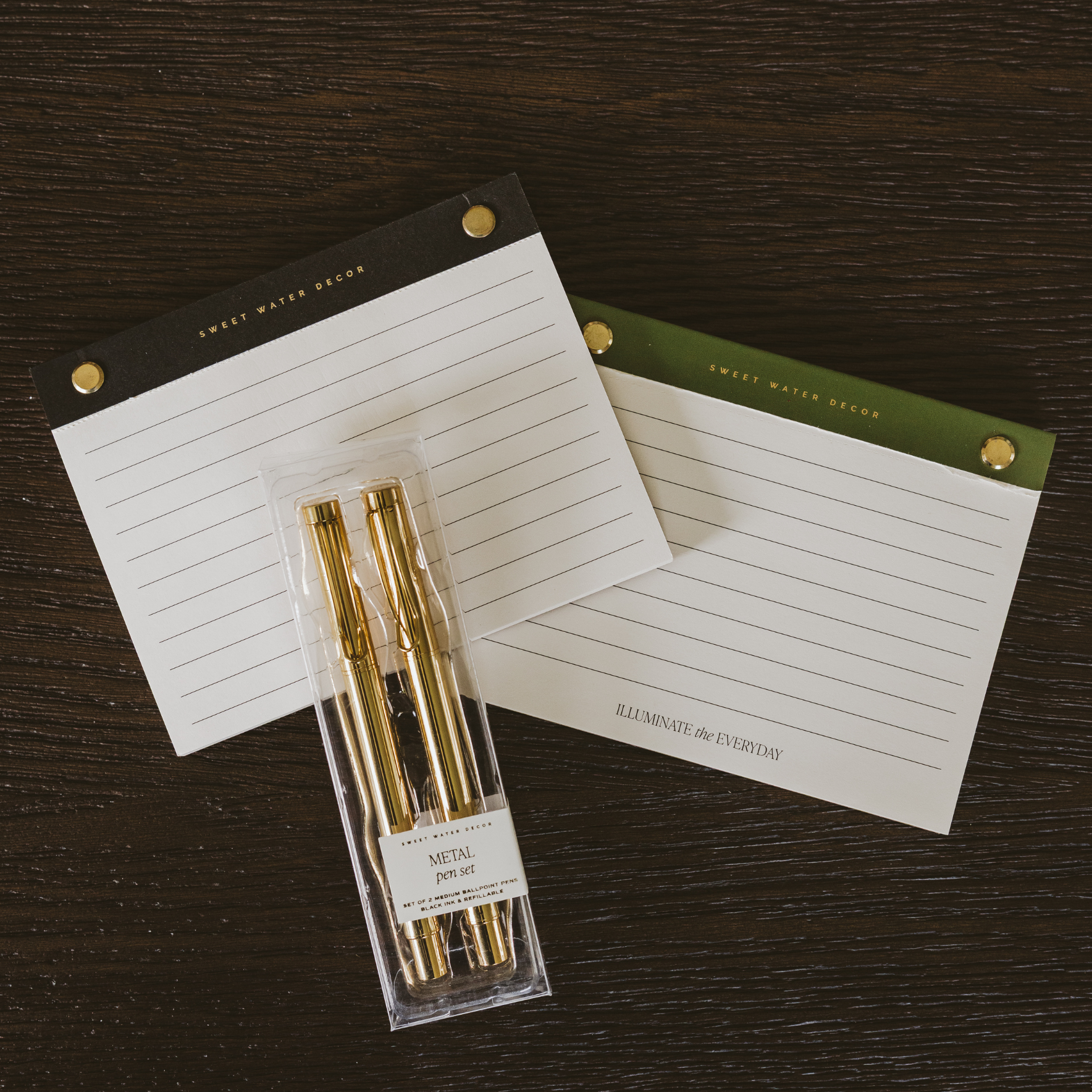 Two notepads with gold pens in packaging on a dark wooden surface