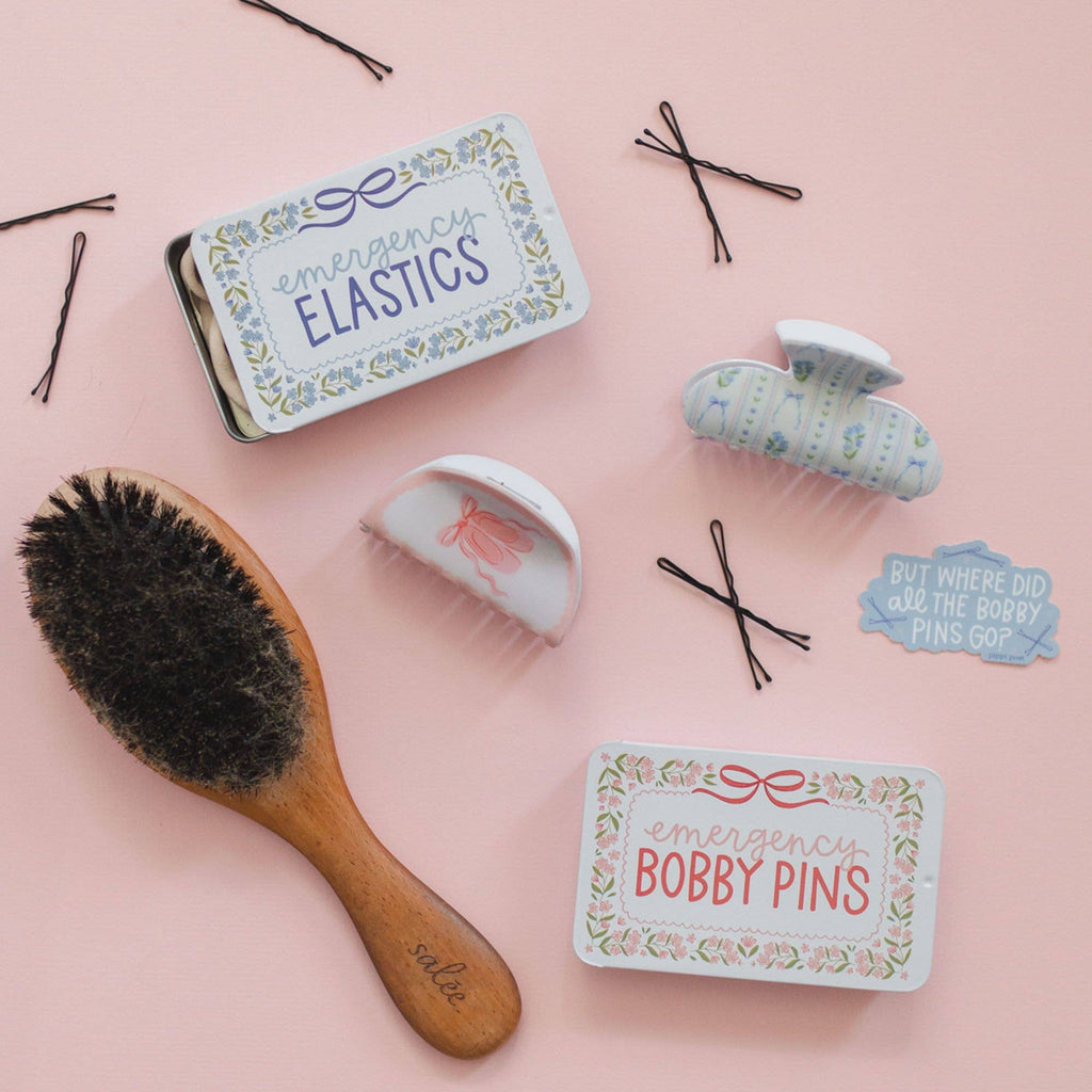 Hair care products including a brush, hair clips, and tins on a pink background
