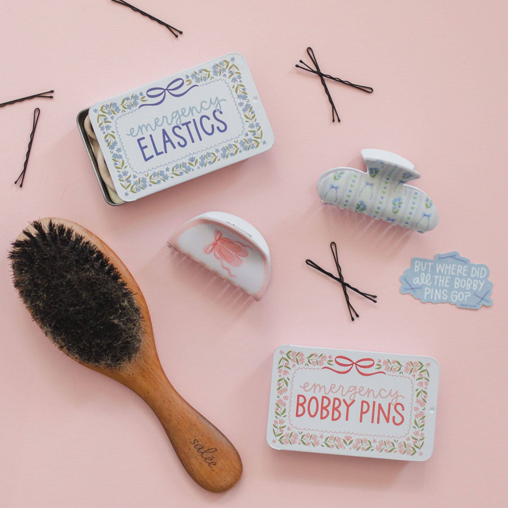 Hair care products including a brush, hair clips, and tins on a pink background