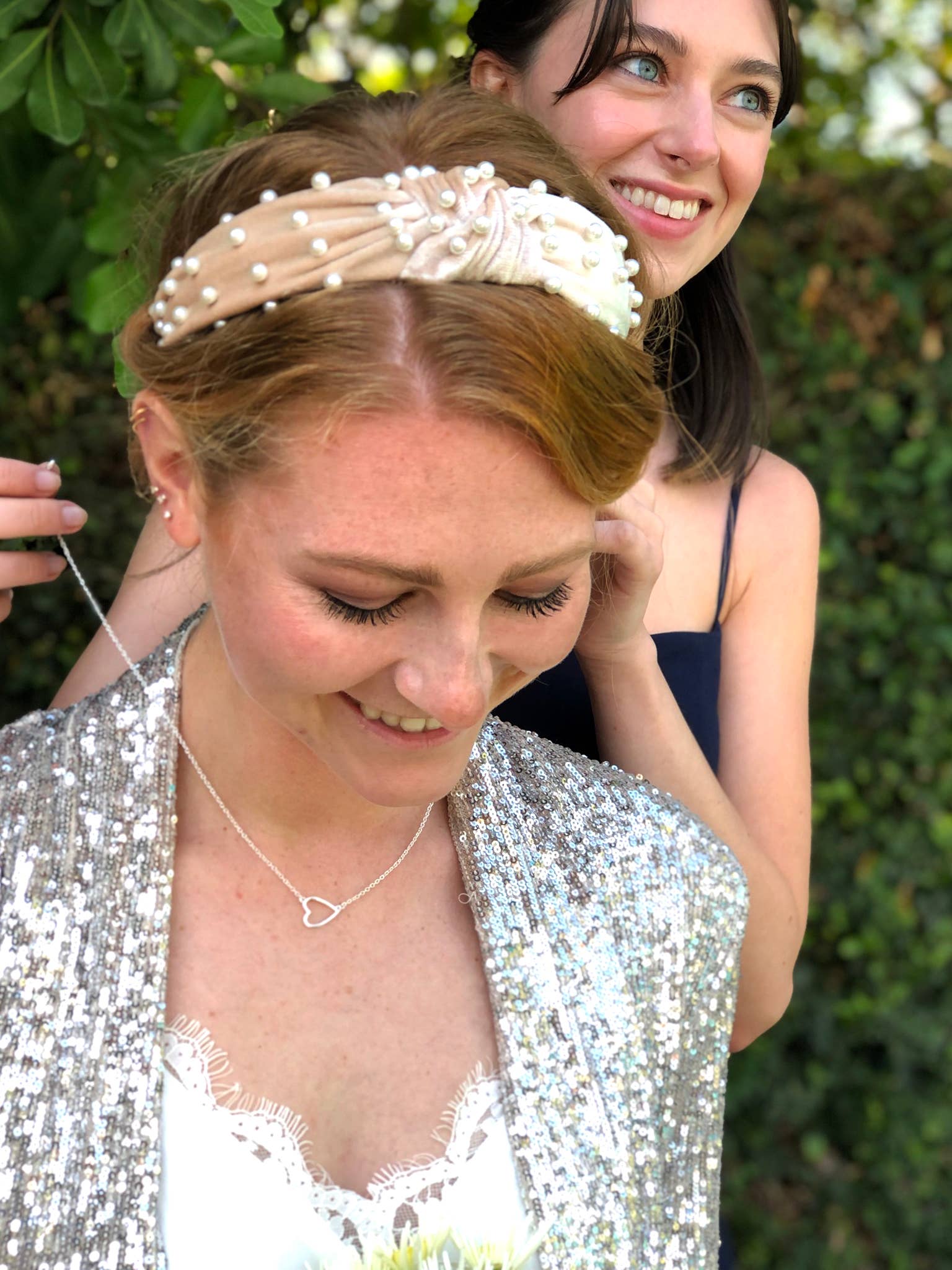 Woman wearing a pearl headband with another woman in the background.