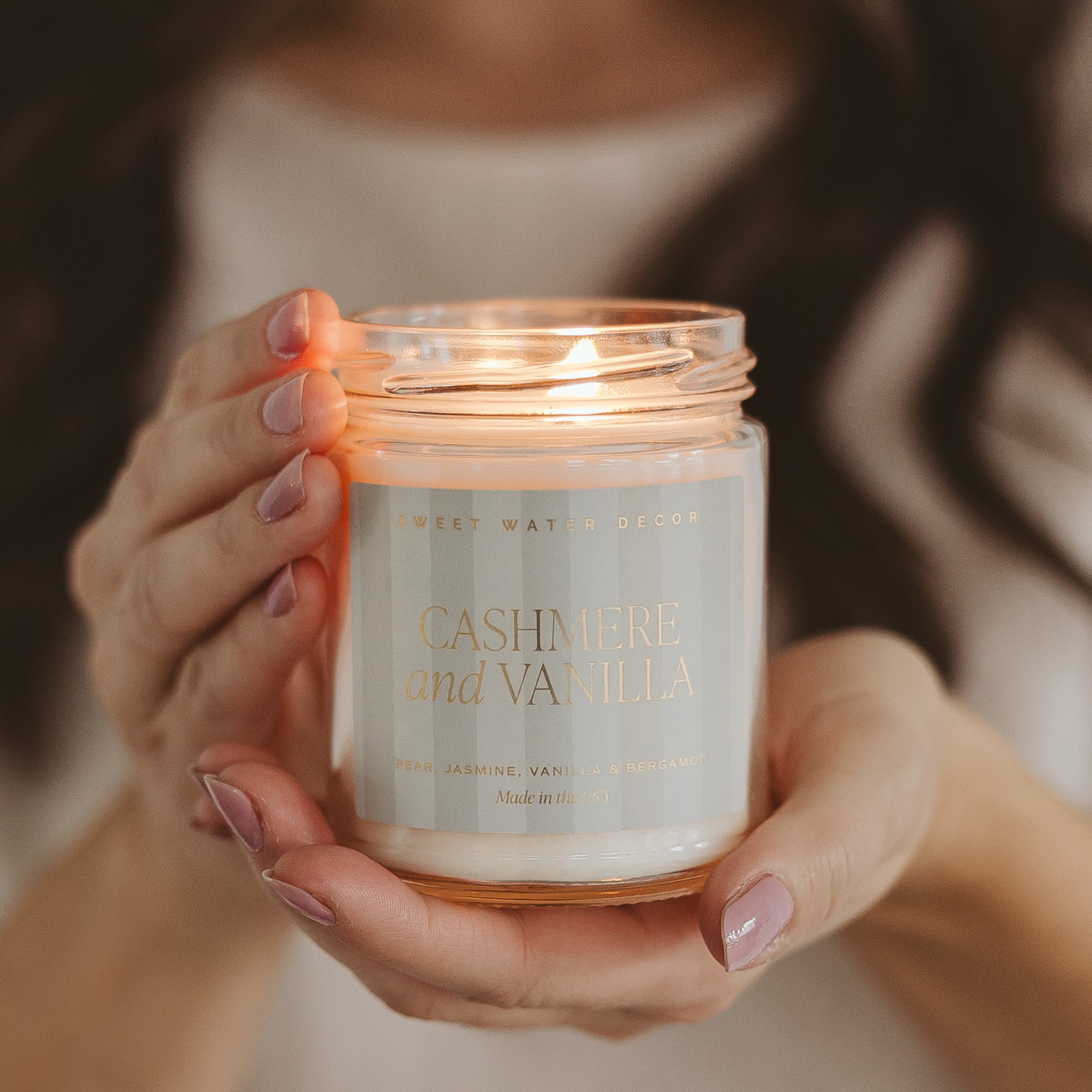 Person holding a candle labeled 'Cashmere and Vanilla' by Sweet Water Decor.
