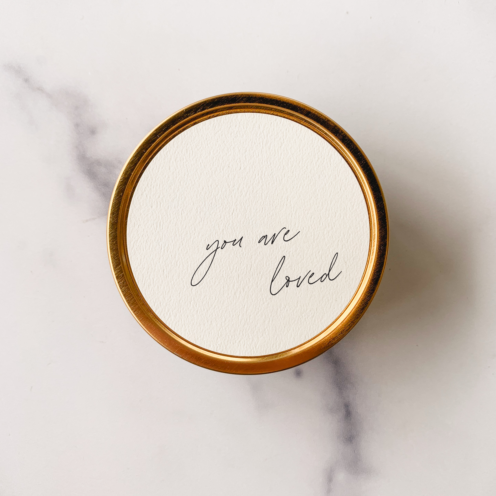 Round white coaster with 'grateful for you' text on a gold rim, placed on a marble surface.