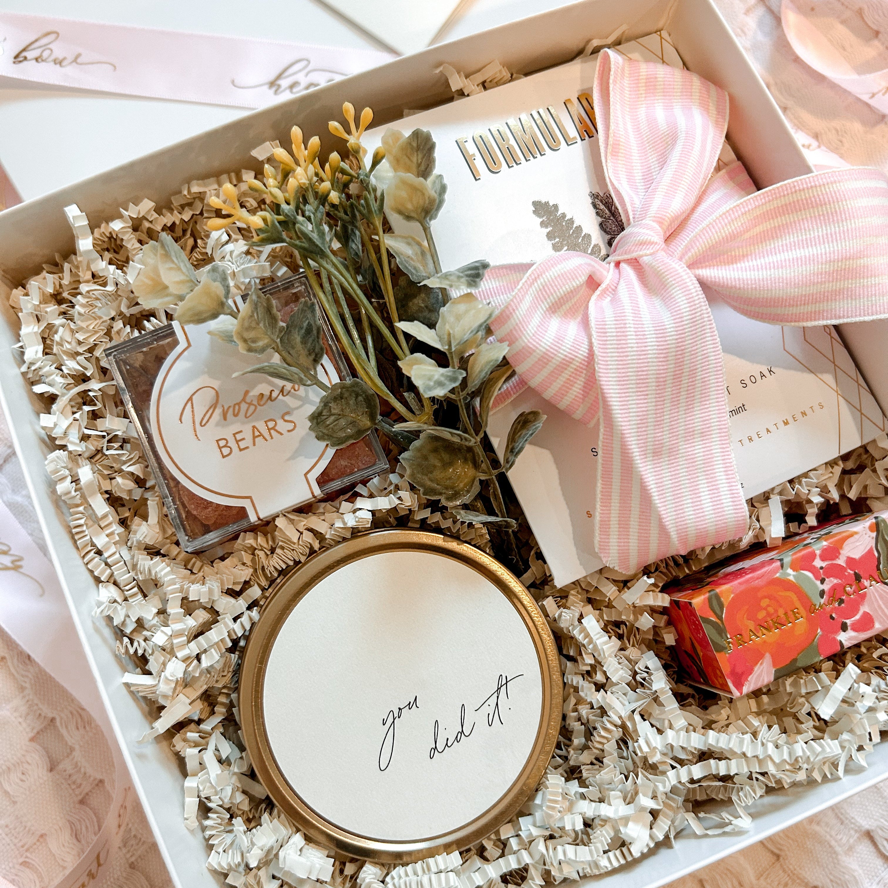 Gift box with decorative items including a small plant, card, and decorative item on a light background.