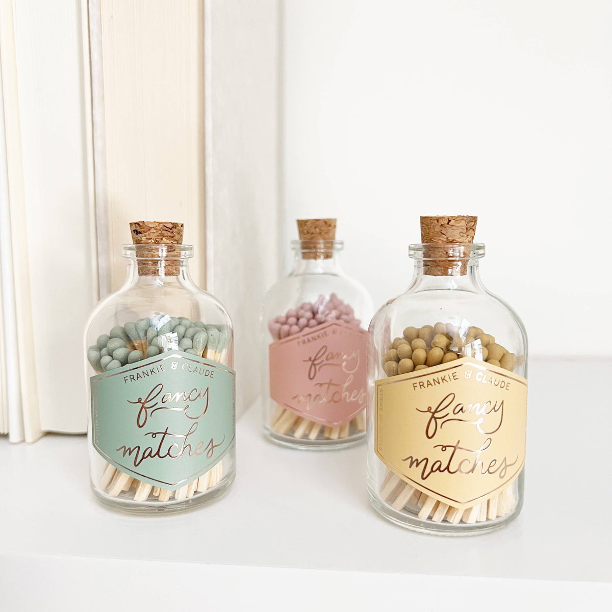 Three decorative glass jars with cork lids on a white surface.