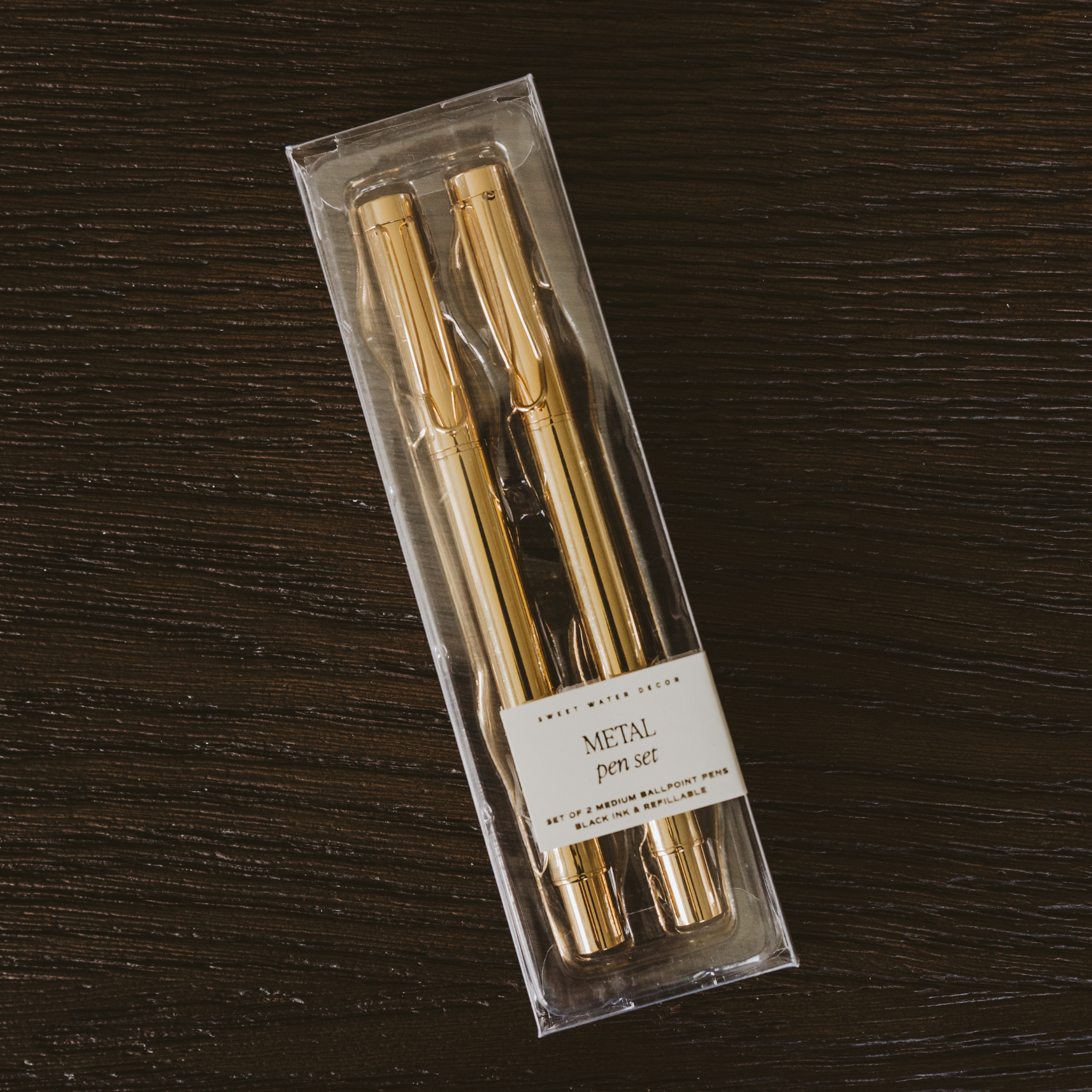 Set of gold pens in clear packaging on a dark wooden surface