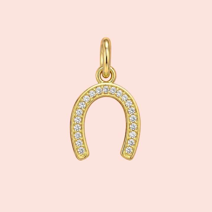 Gold horseshoe-shaped pendant with embedded stones on a pink background