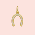 Gold horseshoe-shaped pendant with embedded stones on a pink background