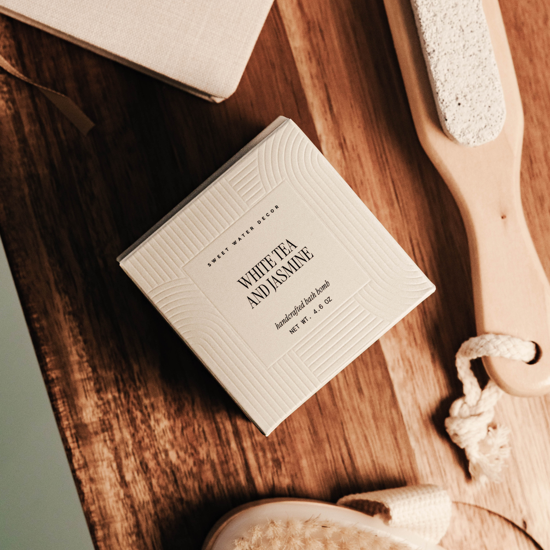 White tea and jasmine soap bar on a wooden surface with a scrubber and loofah.