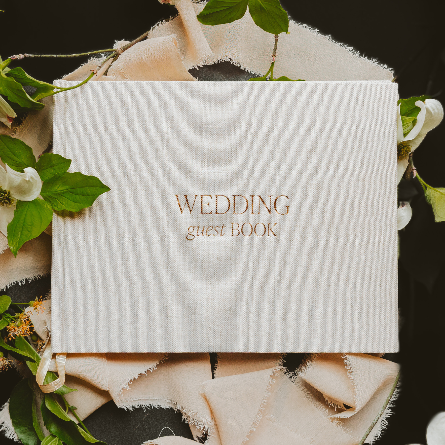White wedding guest book with gold text surrounded by floral and leaf decorations.