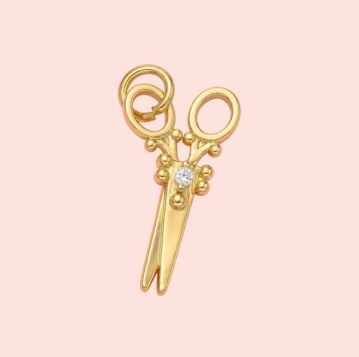 Gold scissors-shaped pendant with a diamond on a pink background