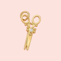 Gold scissors-shaped pendant with a diamond on a pink background