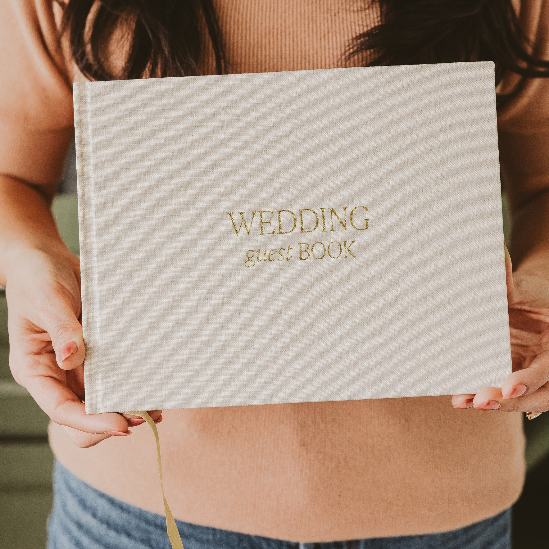 Person holding a beige wedding guest book with gold text.
