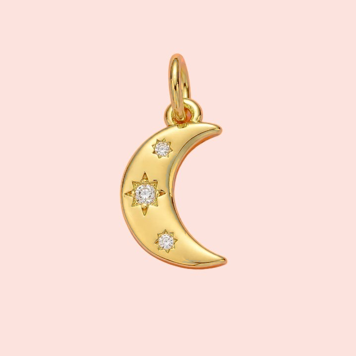 Gold crescent moon pendant with embedded diamonds on a pink background