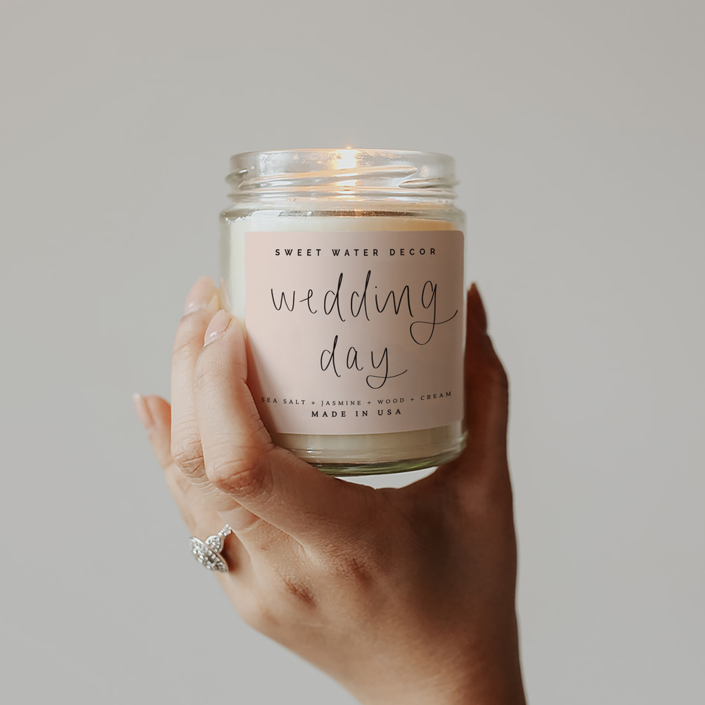 Hand holding a 'wedding day' scented candle with a soft pink label against a neutral background
