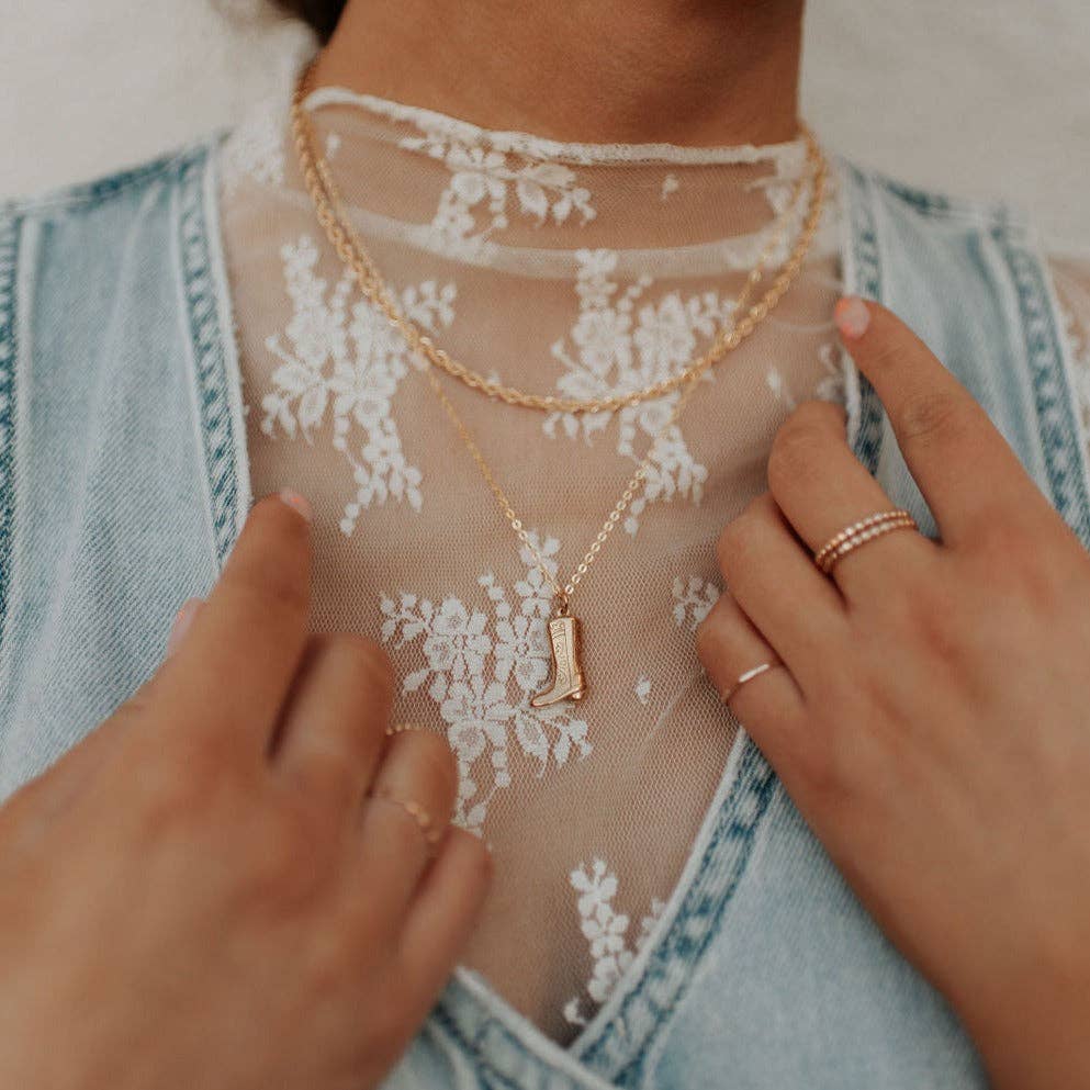 Close-up of a person wearing a gold necklace with a pendant, with hands adjusting the garment.