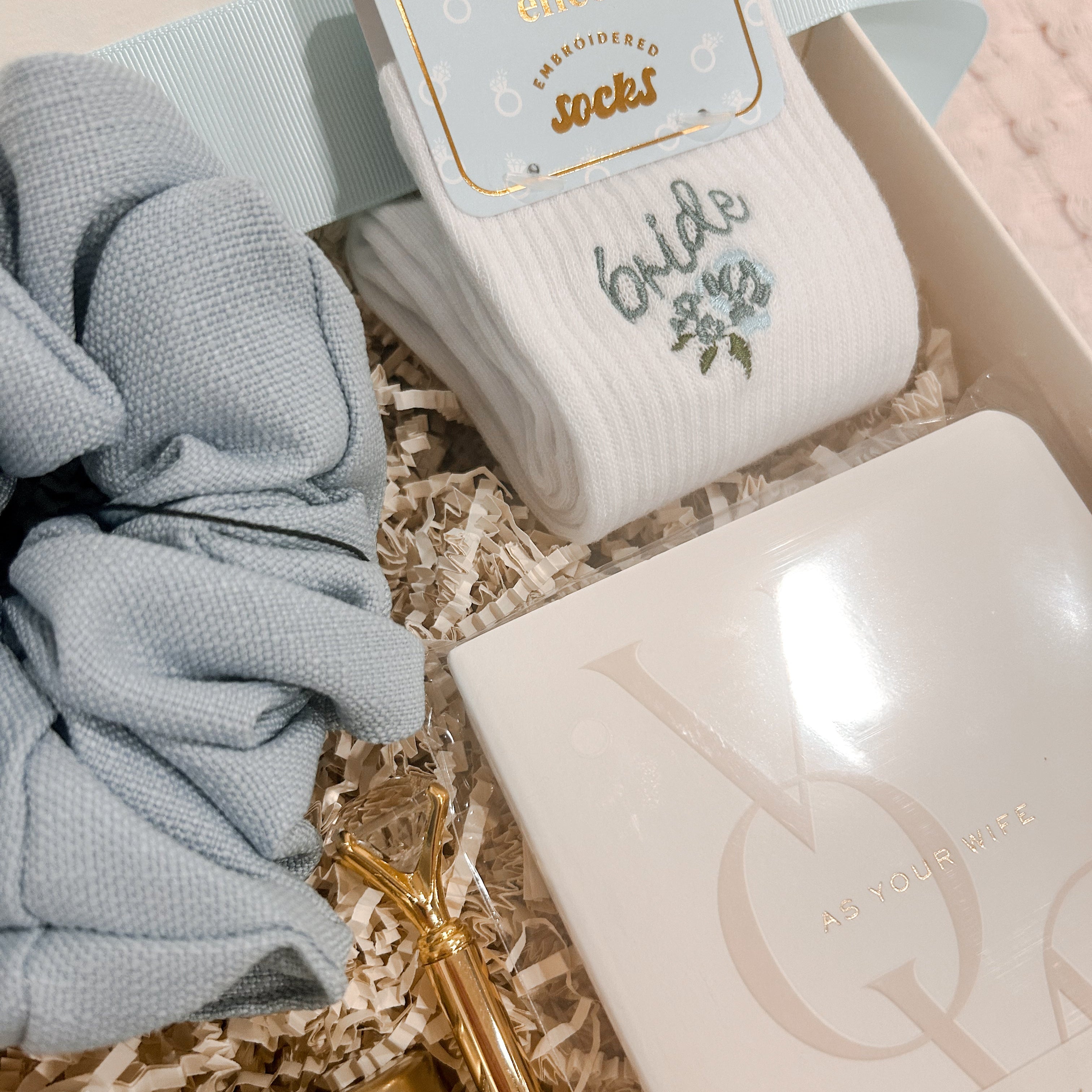 Close-up of Heart & Bow's Something Blue Bride-to-Be Gift Box featuring embroidered bride socks, powder blue jumbo scrunchie, keepsake vow books, and a gold diamond pen for wedding planning.