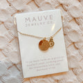 Gold necklace with two round pendants on a Mauve Jewelry Co. card against a textured beige background