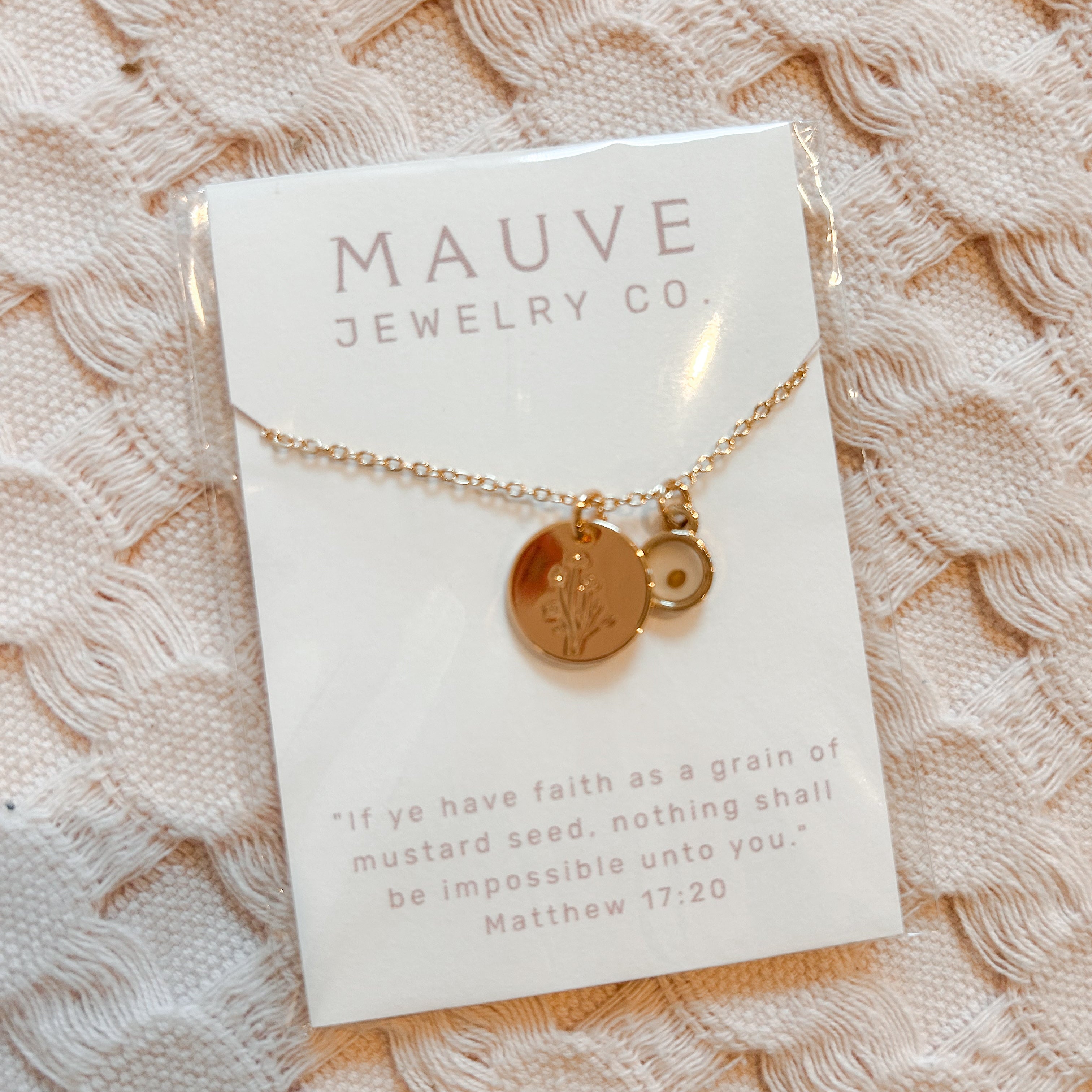 Gold necklace with two round pendants on a Mauve Jewelry Co. card against a textured beige background