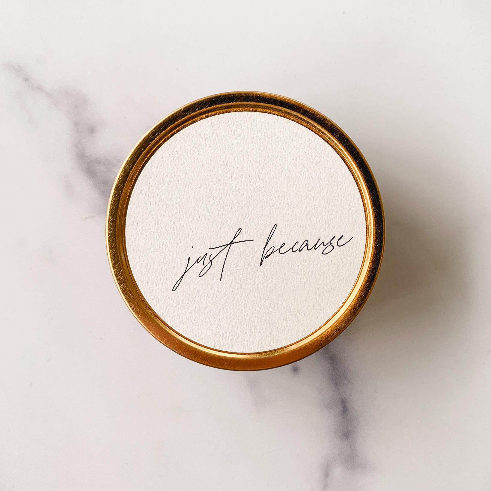 Round white container with gold rim and 'just because' text on a marble background
