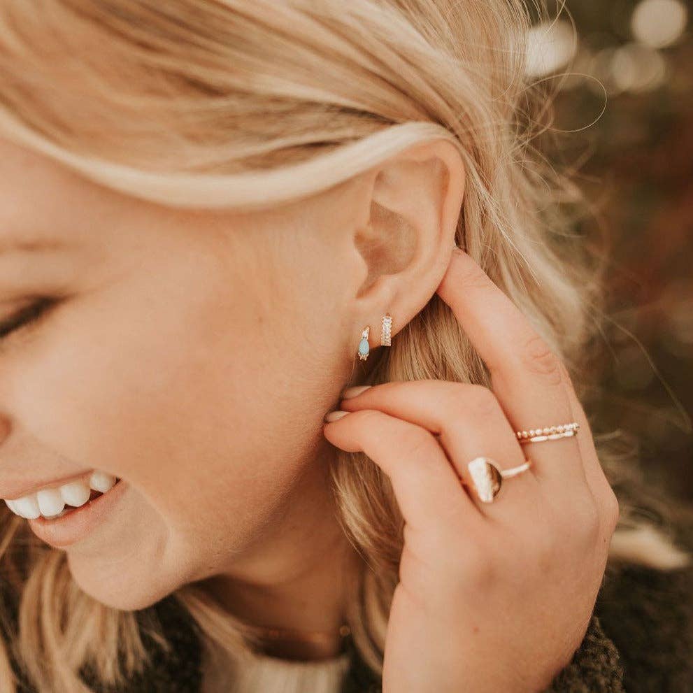 Close-up of a woman wearing multiple earrings and rings, with a blurred natural background.