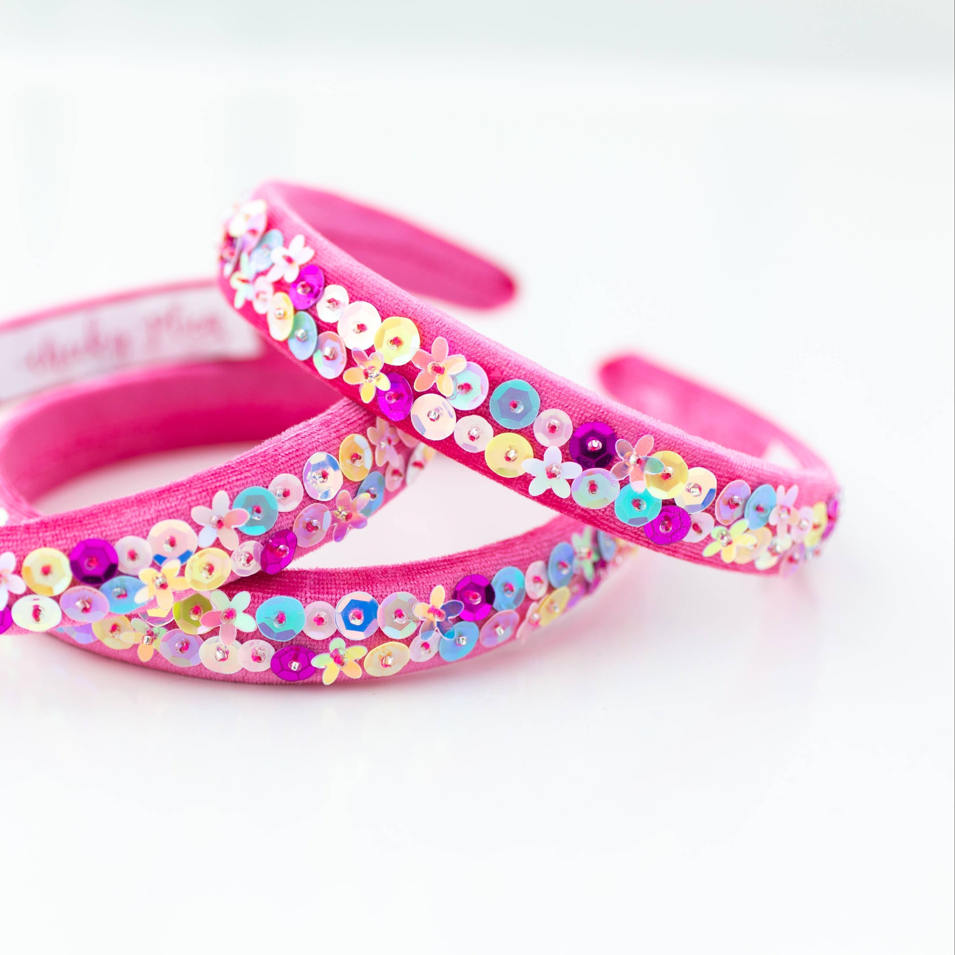 Pink headbands with colorful sequin flowers on a white background