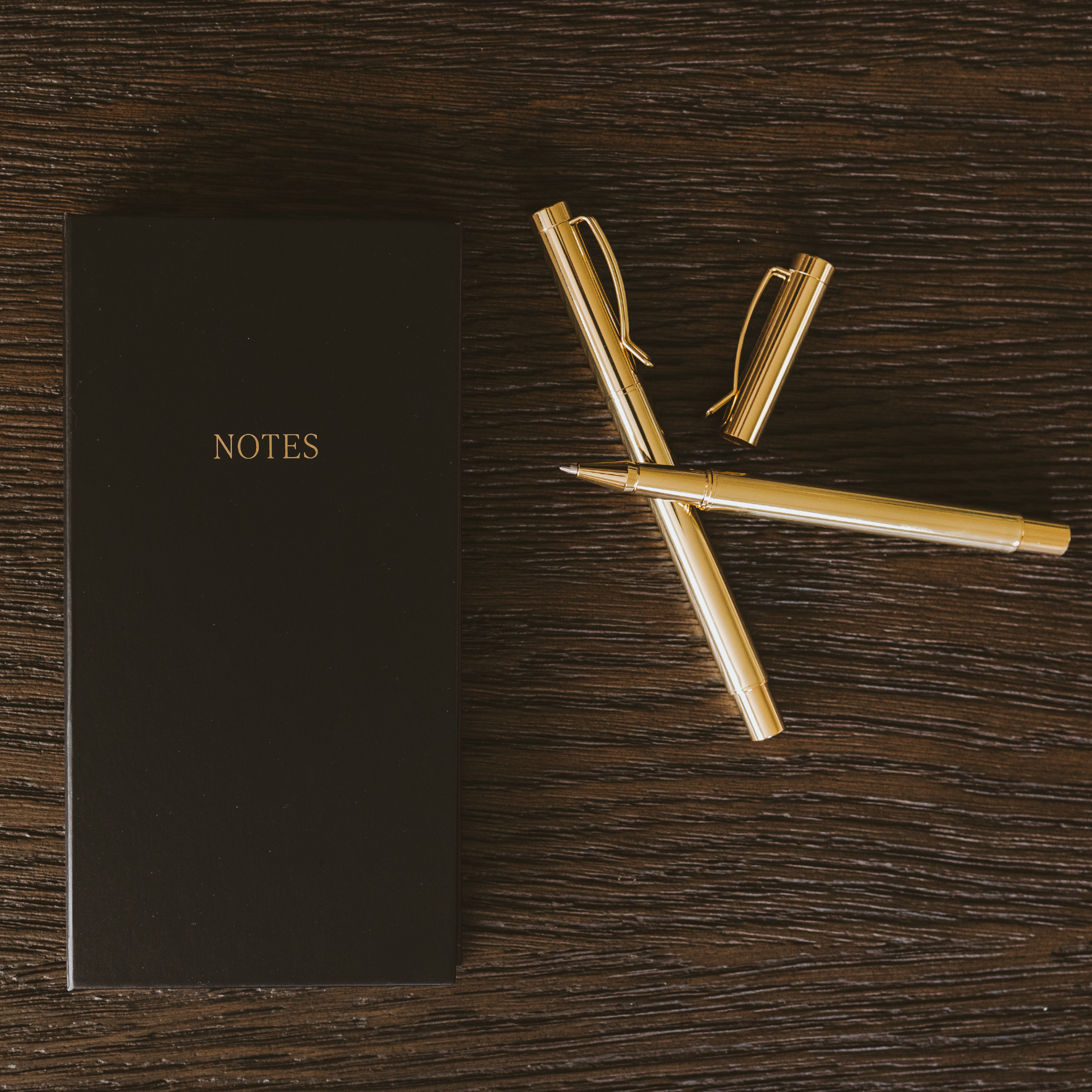 Black notebook labeled 'NOTES' with gold pens on a wooden surface