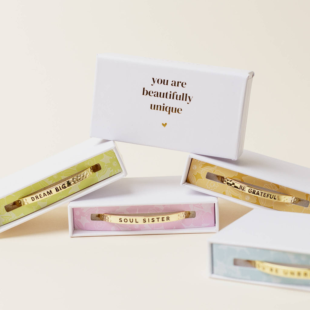 Gold bracelets with motivational phrases in open gift boxes on a light background