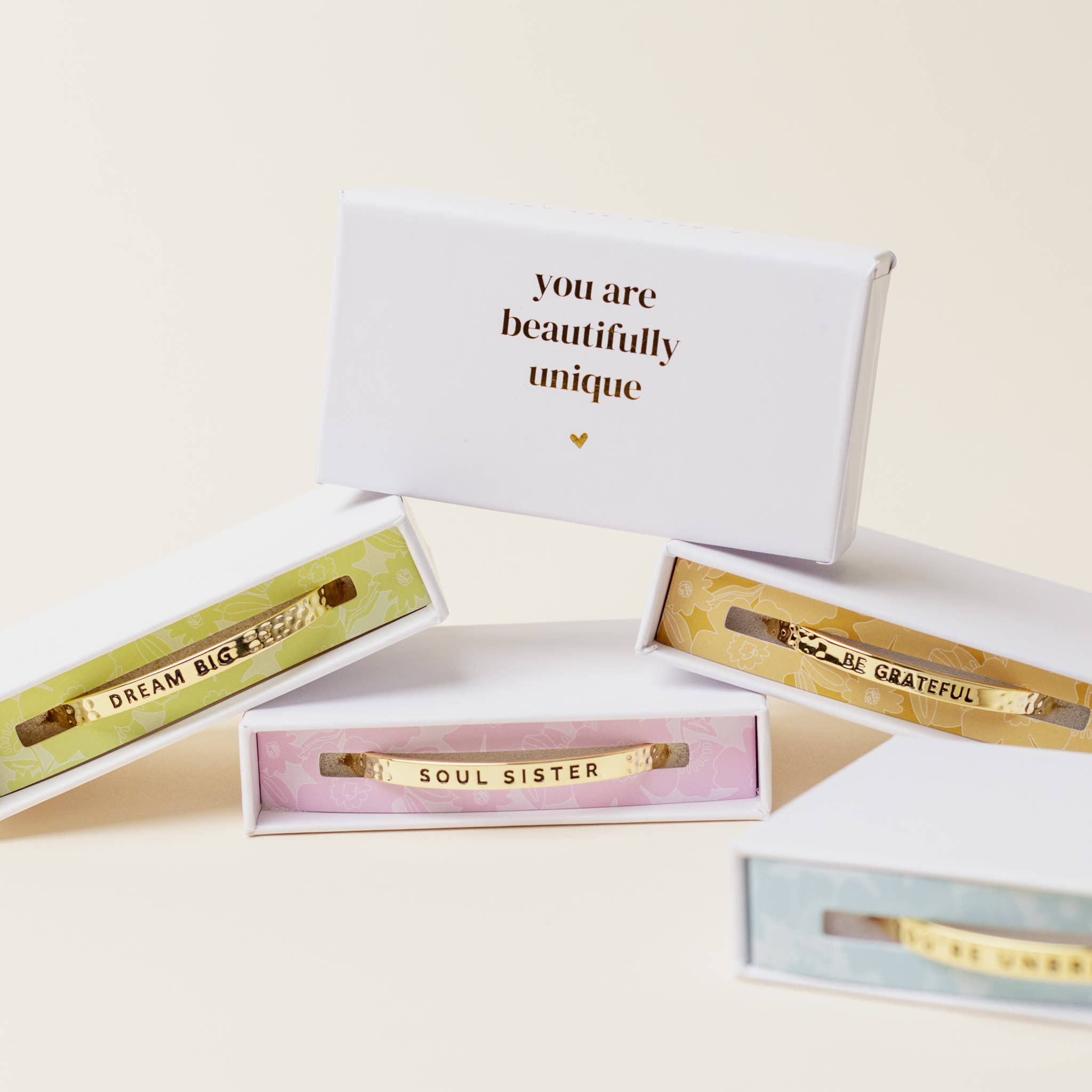 Gold bracelets with motivational phrases in open gift boxes on a light background