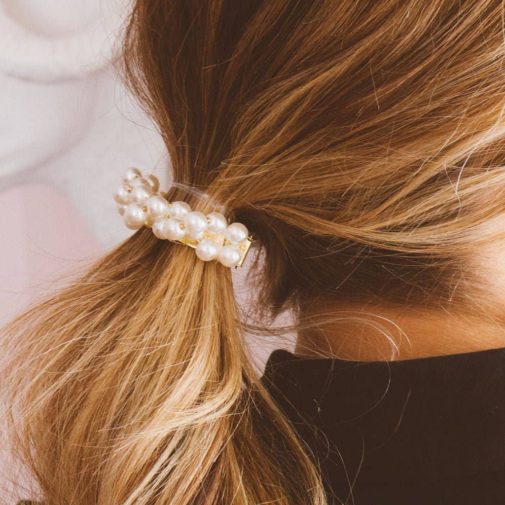 Close-up of a ponytail with a pearl hair tie against a blurred background