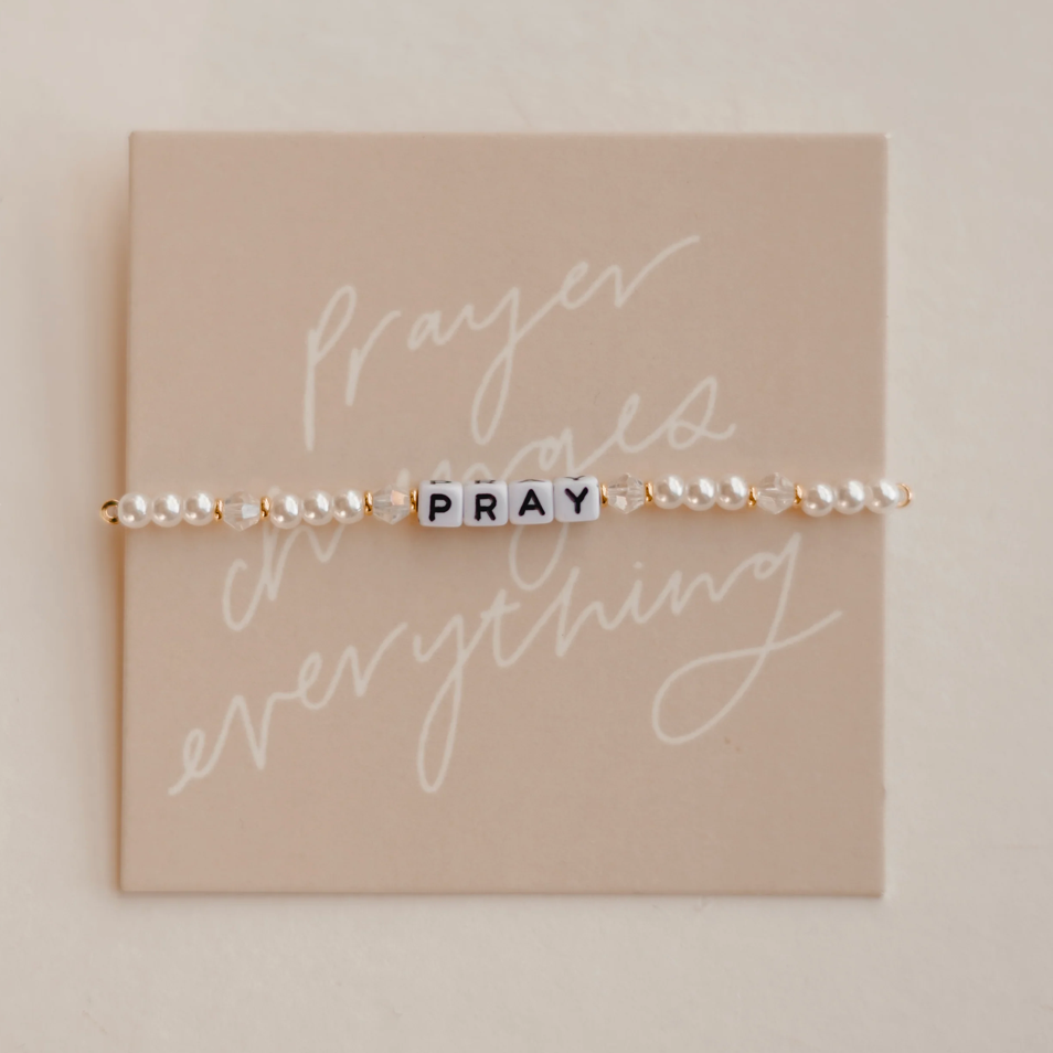 Bracelet with 'PRAY' beads on a beige card with decorative text