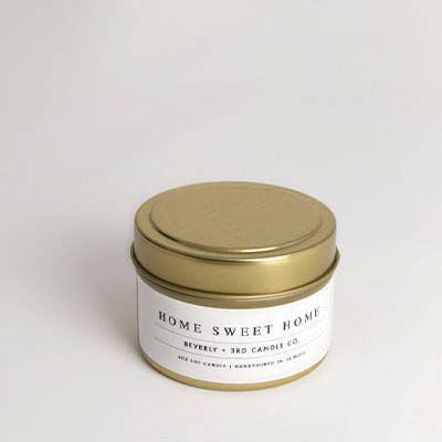Candle in a tin with a gold lid and 'Home Sweet Home' label on a white background