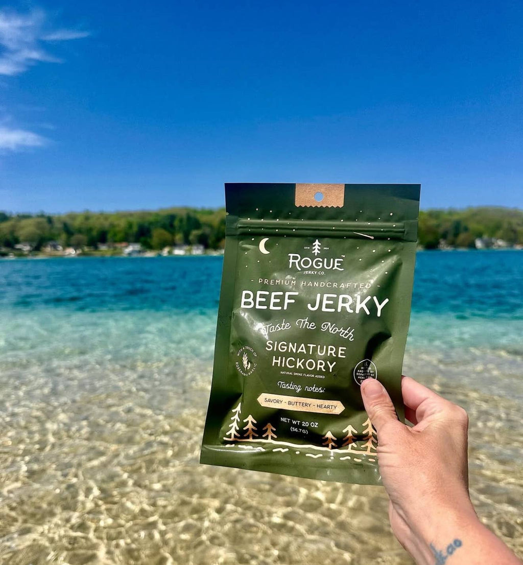 Hand holding a package of Rogue Beef Jerky by a lake