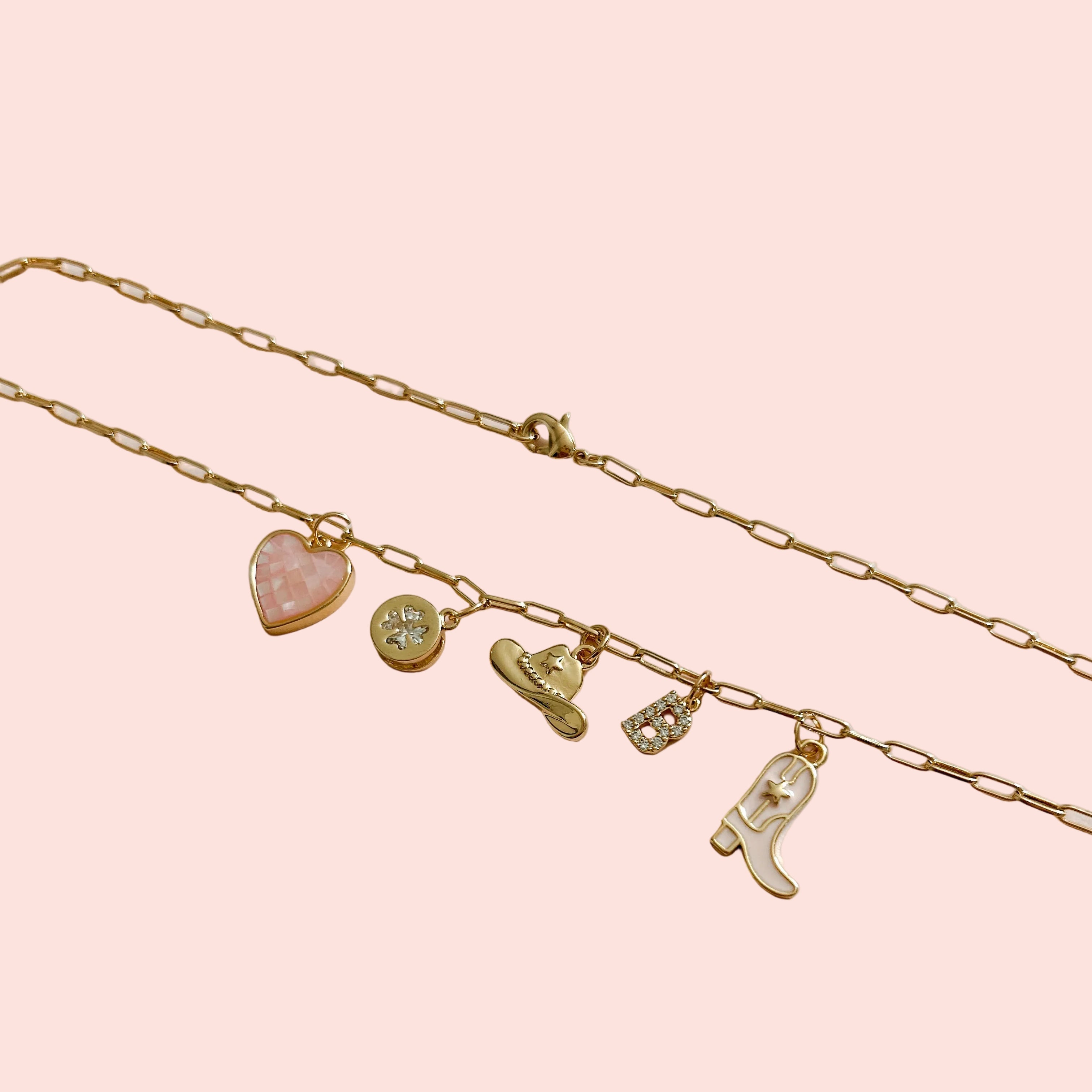 Gold necklace with various charms on a light pink background