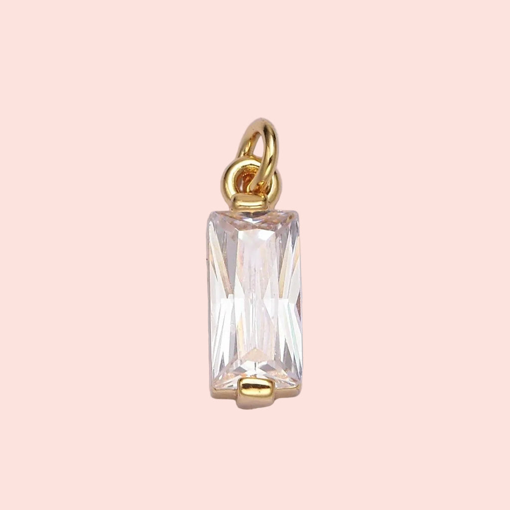 Gold pendant with a rectangular clear gemstone on a light purple background
