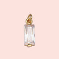 Gold pendant with a rectangular clear gemstone on a light purple background