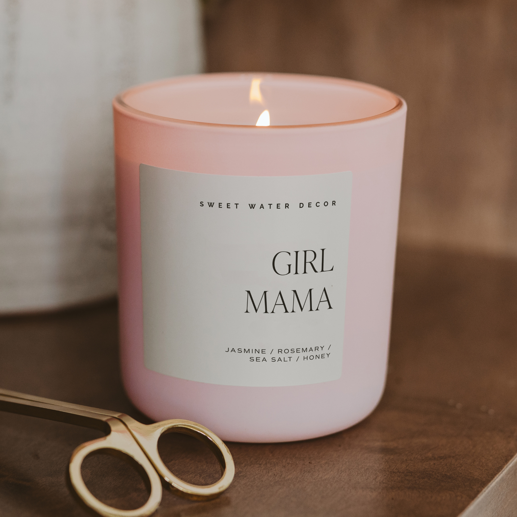 Pink candle labeled 'Girl Mama' with a pair of scissors on a wooden surface