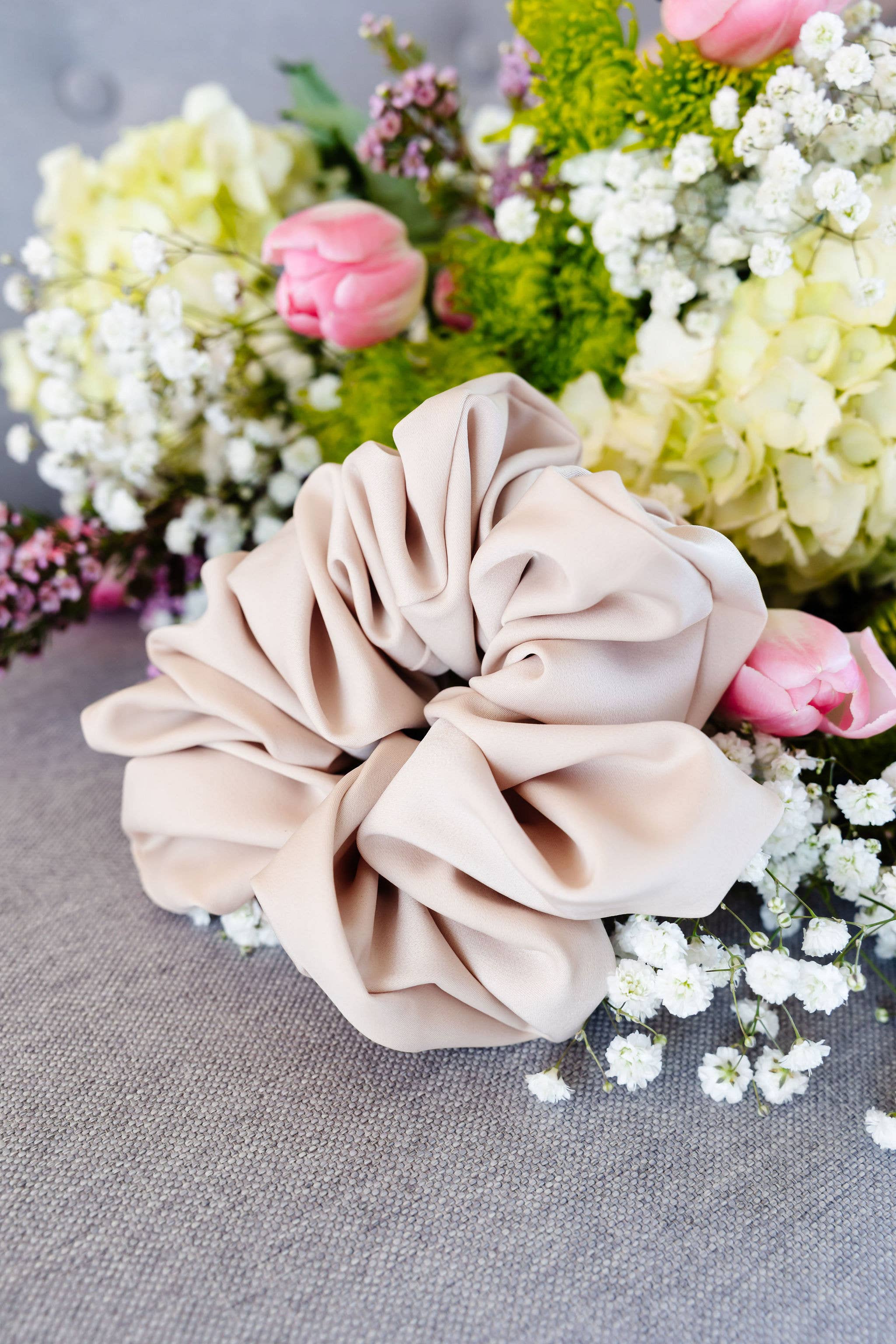 Beige scrunchie on a gray surface with flowers in the background