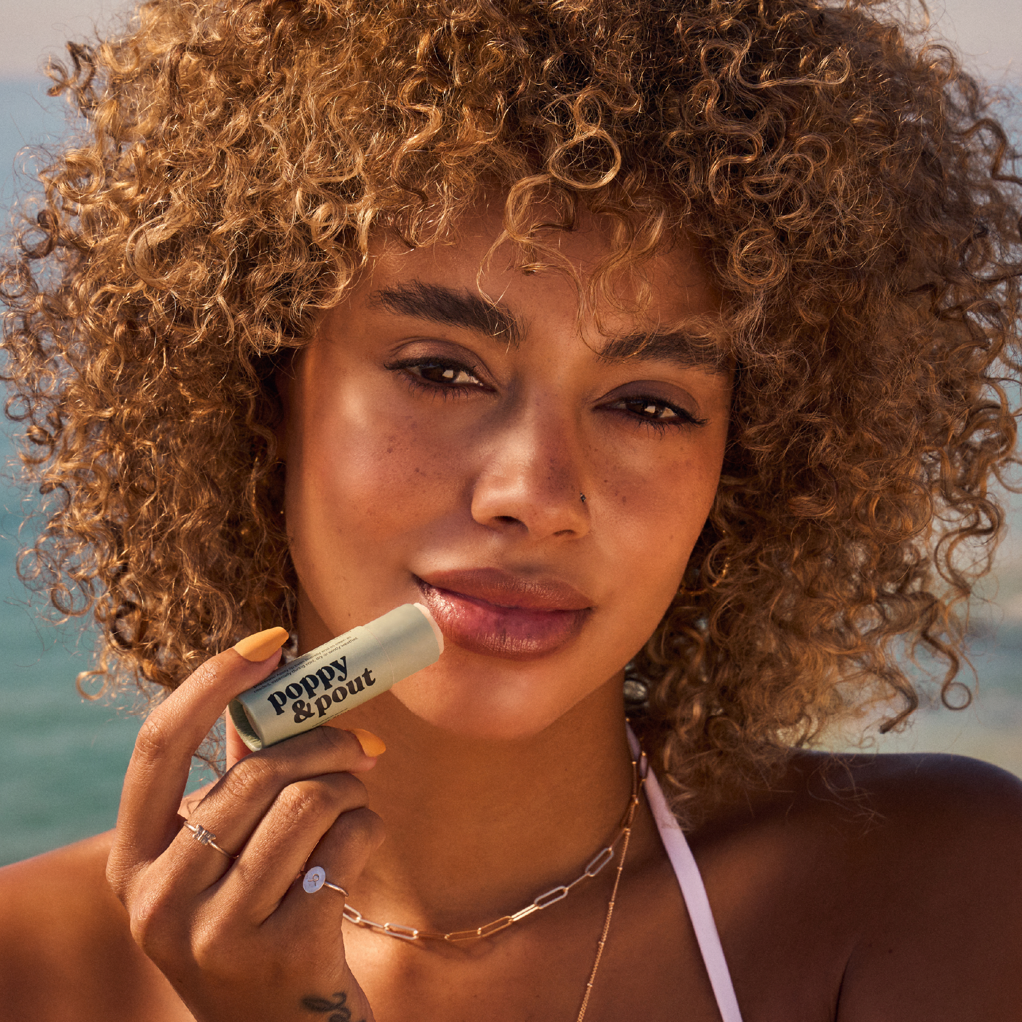 Woman holding a lip balm with a beach background