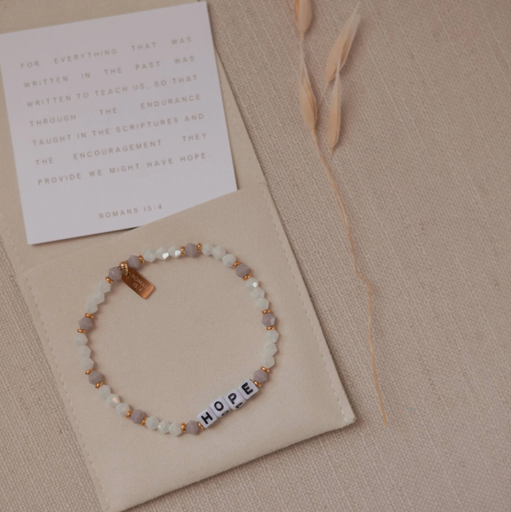 Bracelet with 'HOPE' beads on a beige card with feathers and a letter on a textured surface