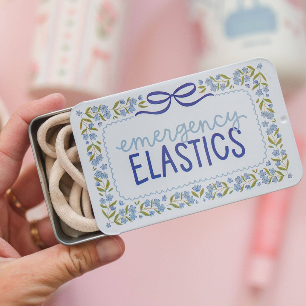 Small tin labeled 'emergency elastics' held by a hand against a blurred background