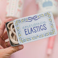 Small tin labeled 'emergency elastics' held by a hand against a blurred background