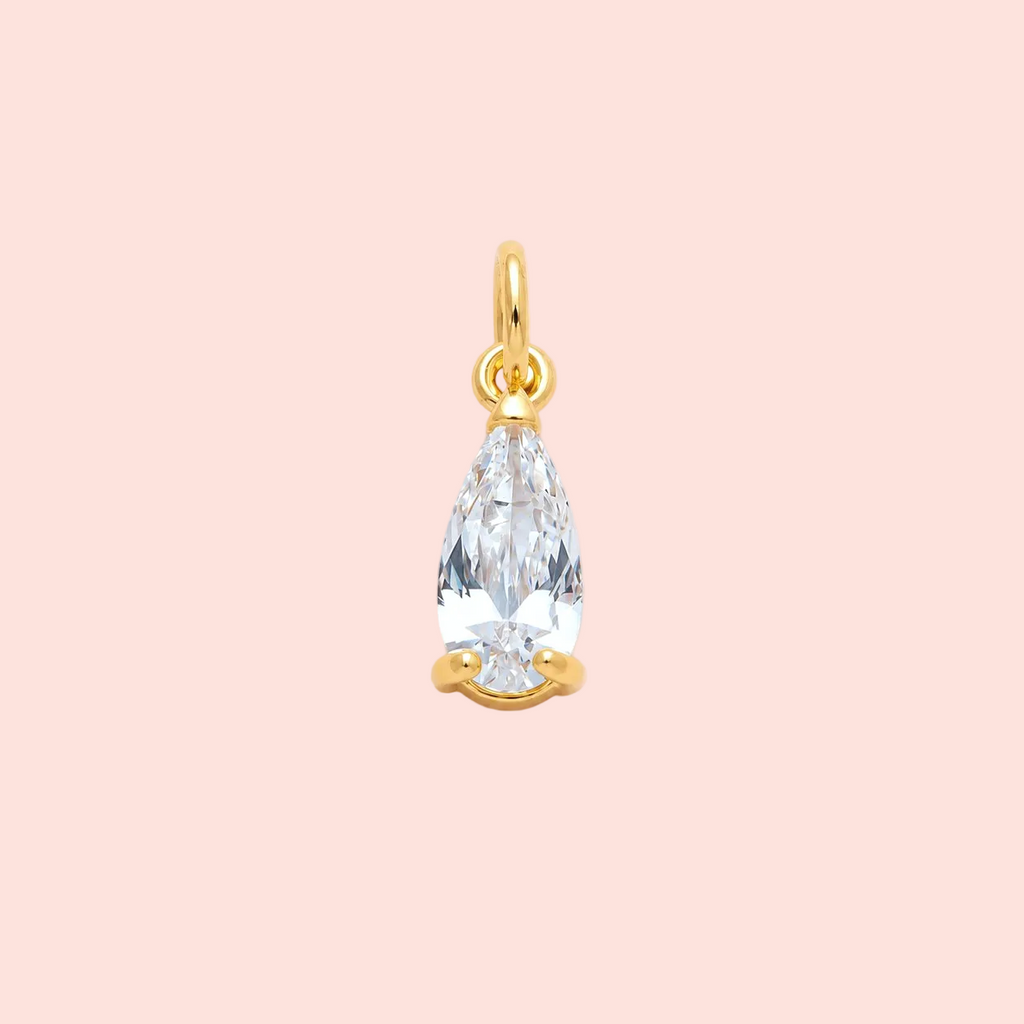 Gold pendant with a clear teardrop-shaped gemstone on a pink background