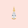 Gold pendant with a clear teardrop-shaped gemstone on a pink background