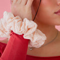 Woman wearing a pink scrunchie on her wrist with a pink background