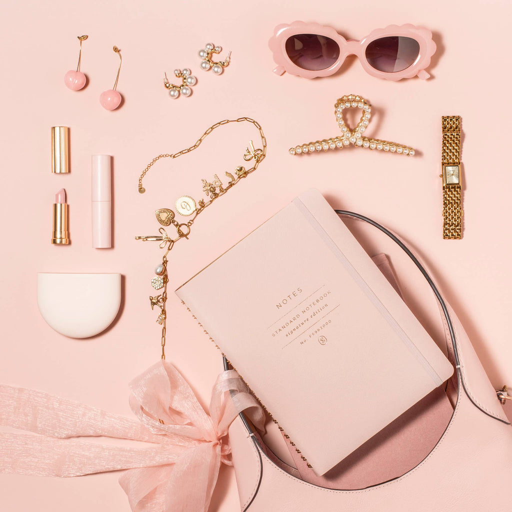 Blush Signature Edition spiral notebook styled with a blush handbag, gold jewelry, pink sunglasses, lipstick, watch, and accessories. A feminine faux leather journal perfect for planning, journaling, work, and everyday inspiration.