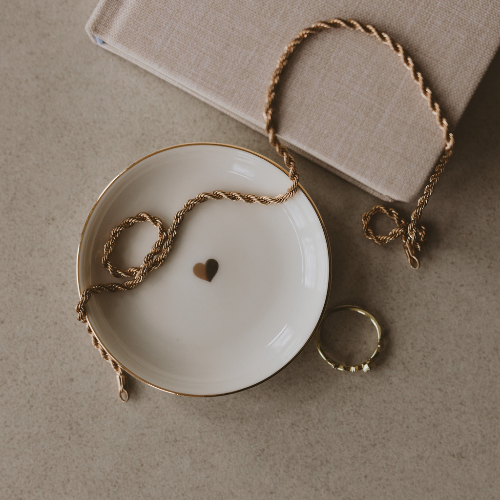 Necklace with heart charm on a white dish, with a beige box in the background