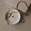 Necklace with heart charm on a white dish, with a beige box in the background