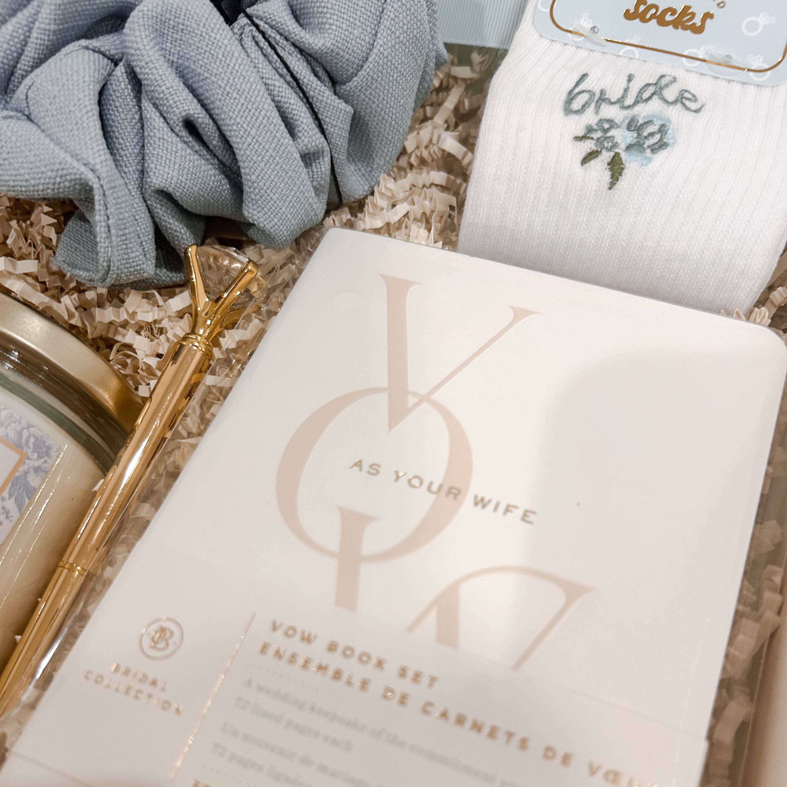 Keepsake wedding vow books paired with embroidered bride socks, a gold diamond pen, powder blue scrunchie, and Something Blue candle in Heart & Bow's luxury bride-to-be gift box.