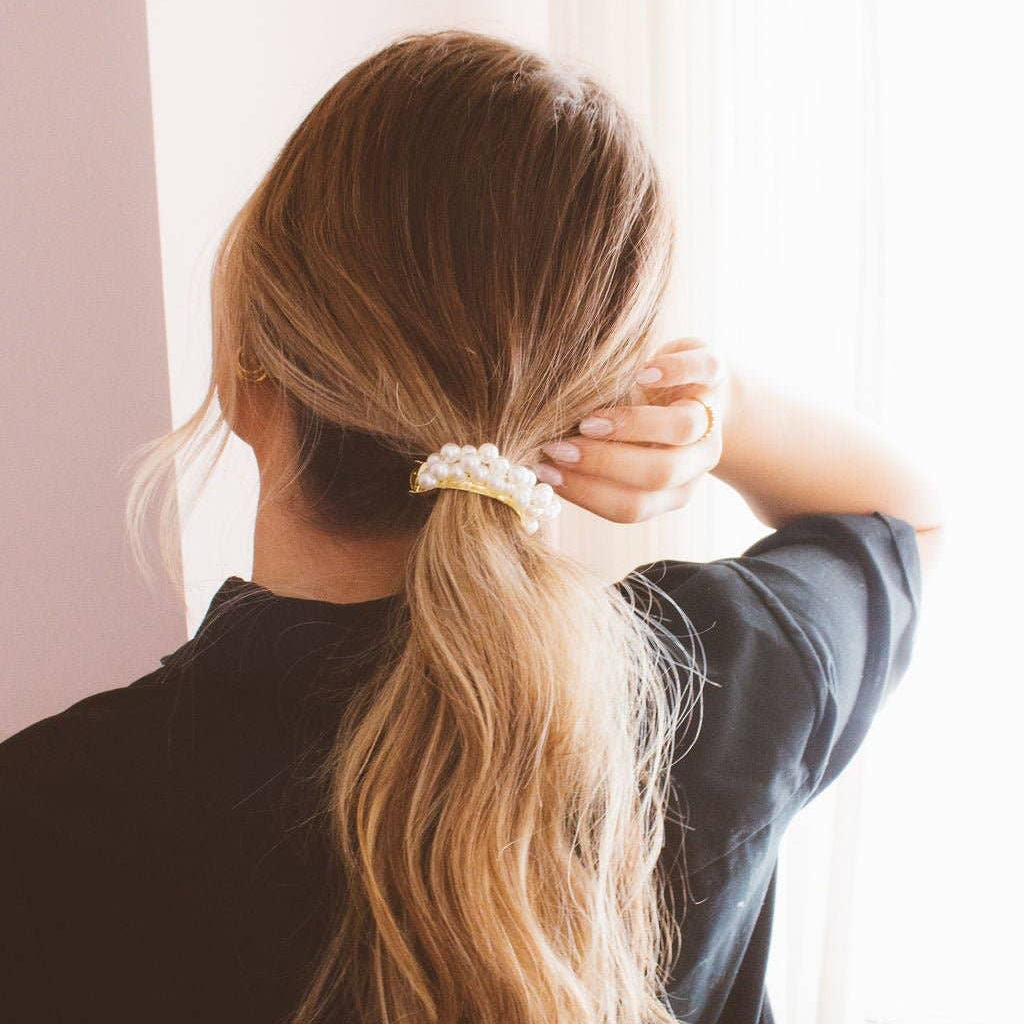 Person with long blonde hair tied in a ponytail with a decorative clip, wearing a black shirt.